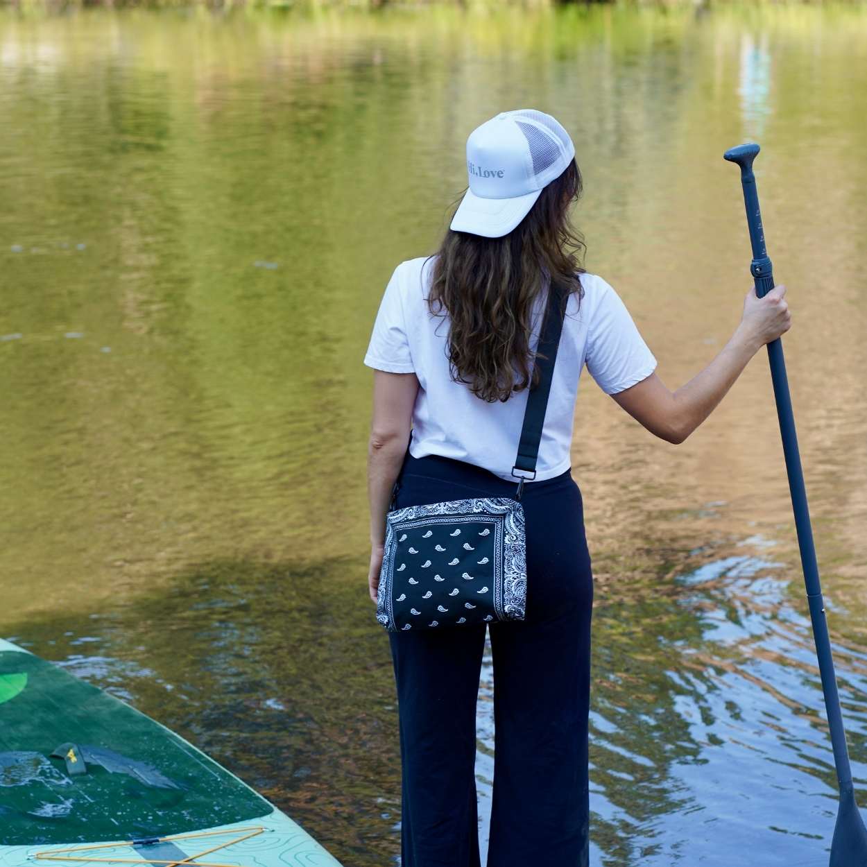 Woman paddleboarding on water with crossbody purse in black bandana print