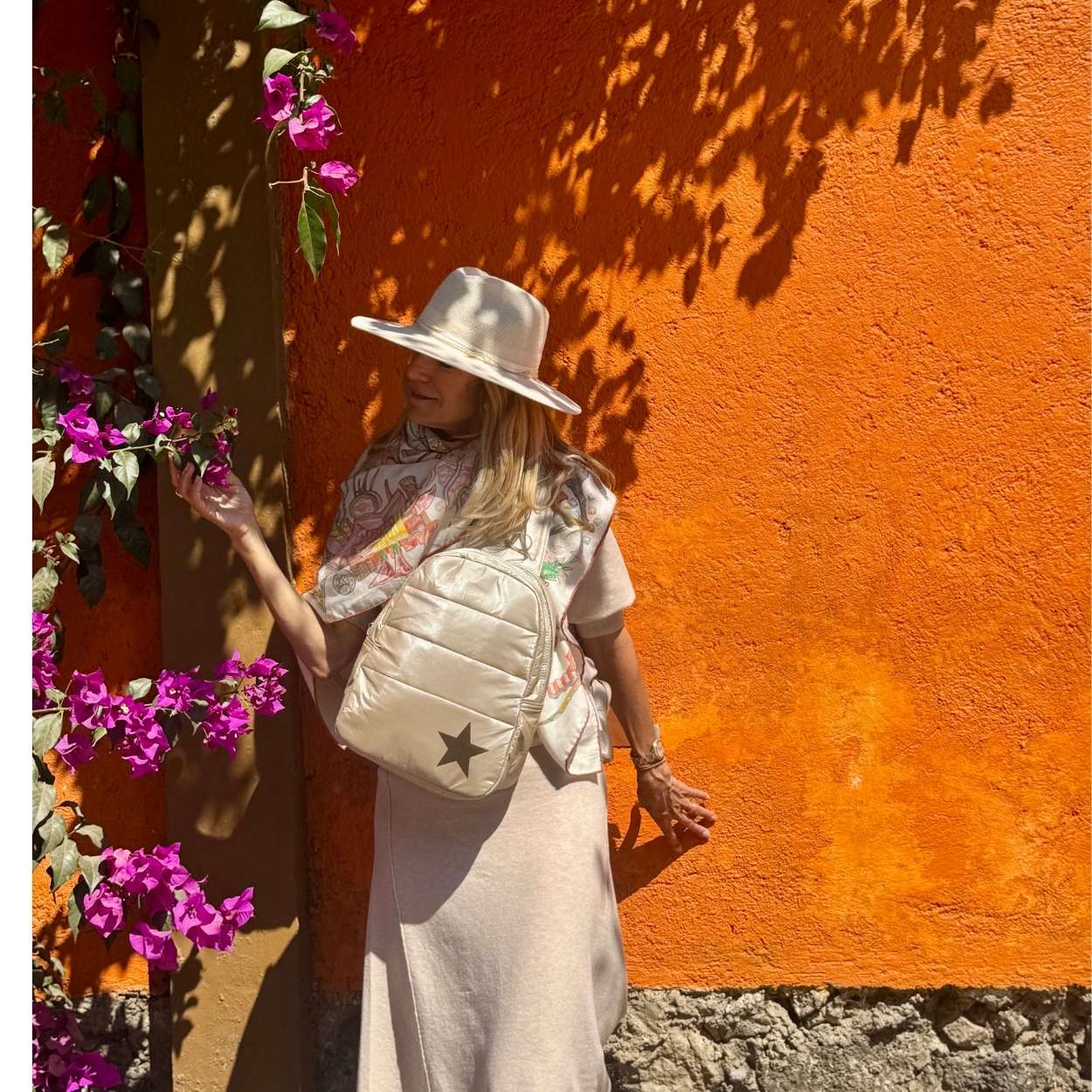 Woman with a shimmer beige backpack against an orange wall with purple flowers