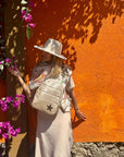 Woman with a shimmer beige backpack against an orange wall with purple flowers