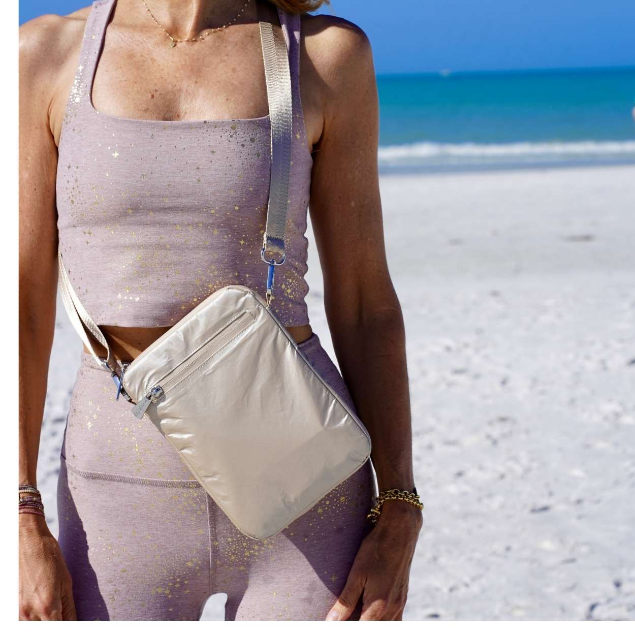 Person wearing a sparkly outfit with a beige crossbody bag on a beach.