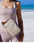 Person wearing a sparkly outfit with a beige crossbody bag on a beach.