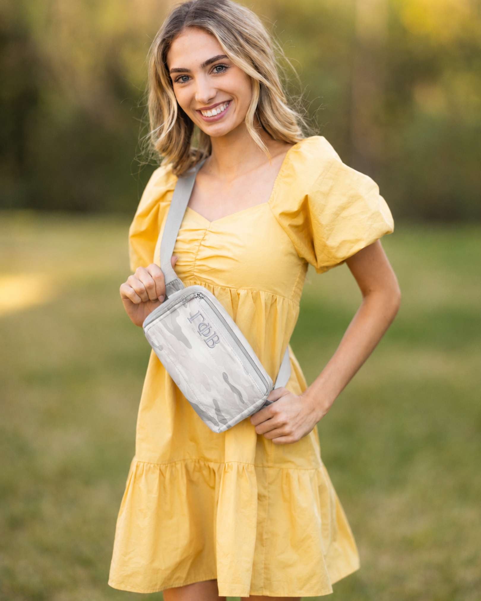 Woman holding a white and Gray Camo-pattern pouch embroidered with Gamma Phi Beta letters.