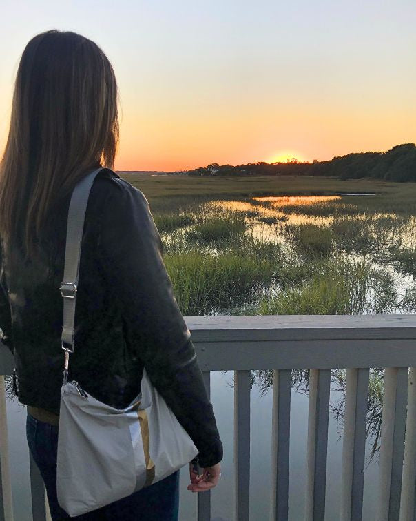 Women standing on a deck admiring the view of the sunset and wearing a gray striped purse.