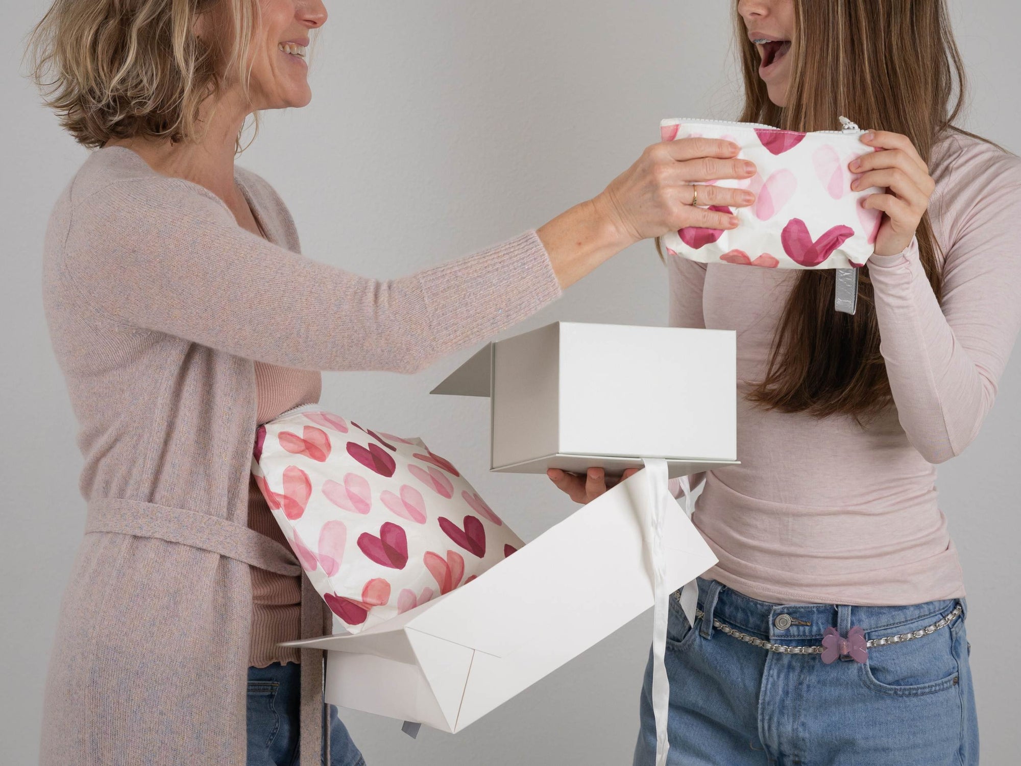 Two women opening a gift box with a heart-patterned bag inside.