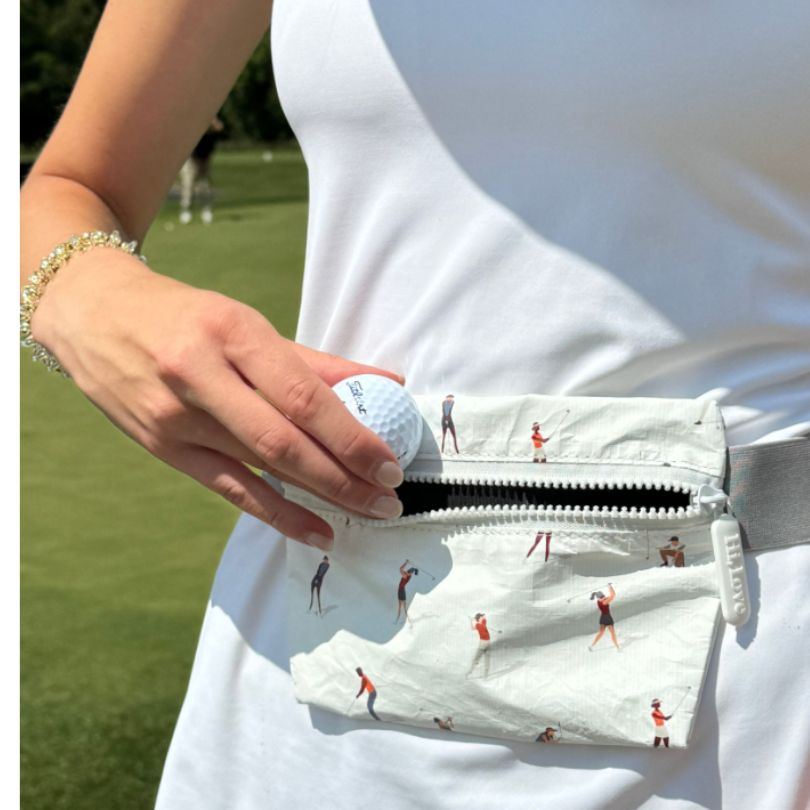 Person putting golf ball into layflat fanny pack belt bag in golfers pattern