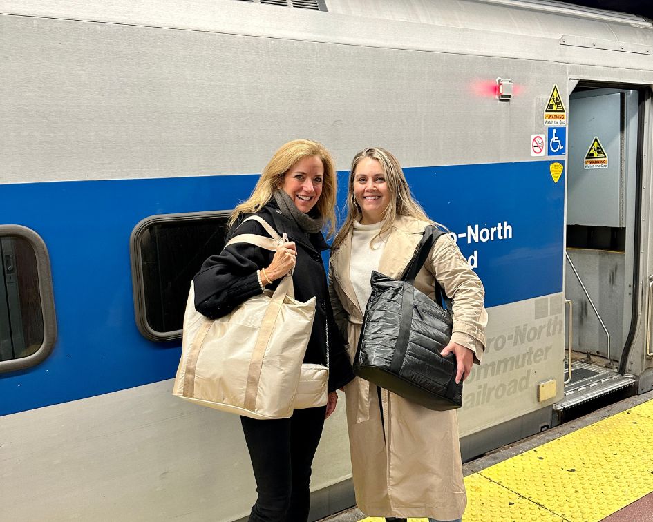 Two women standing by train holding tote bags