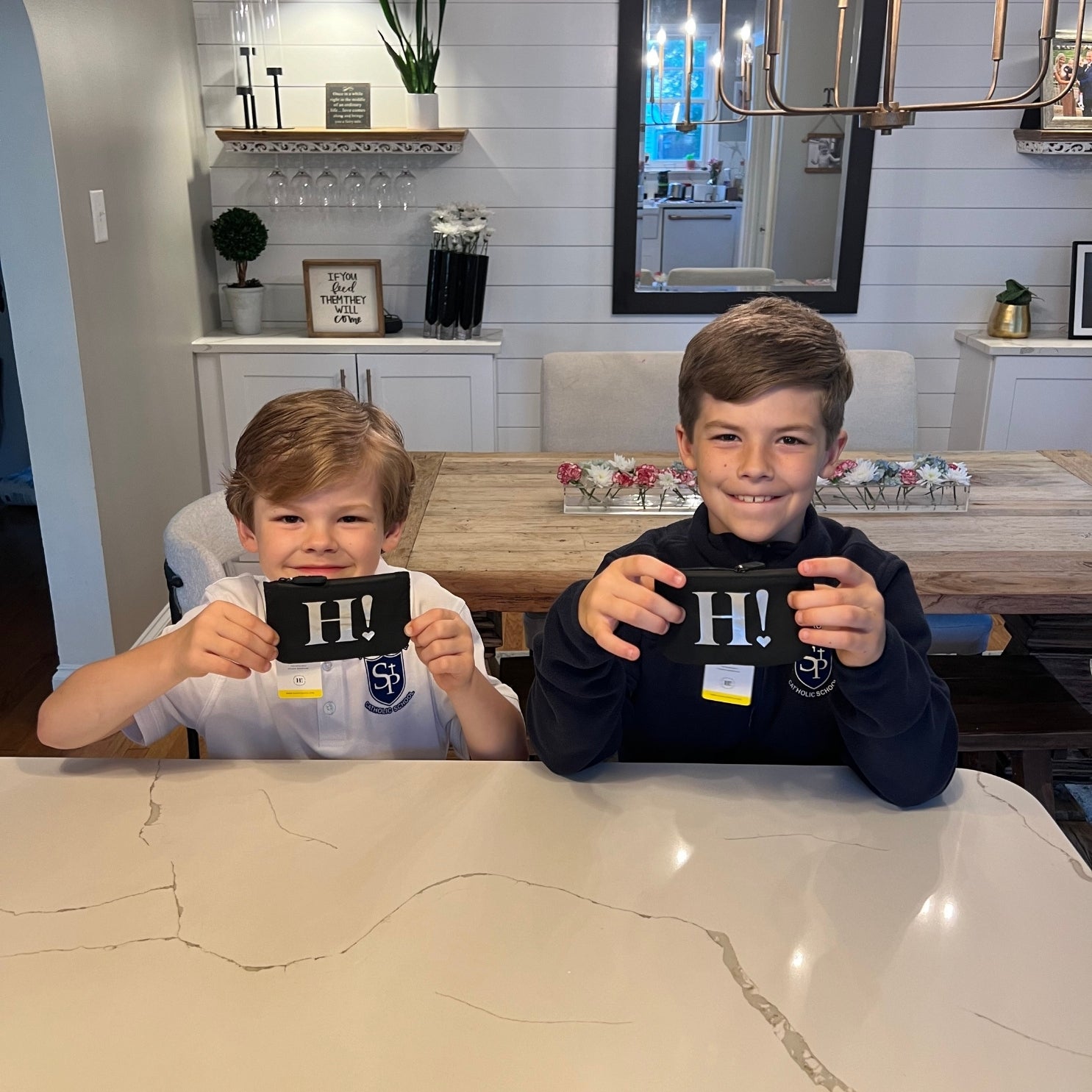 Two children smiling holding black card pouches with silver H!
