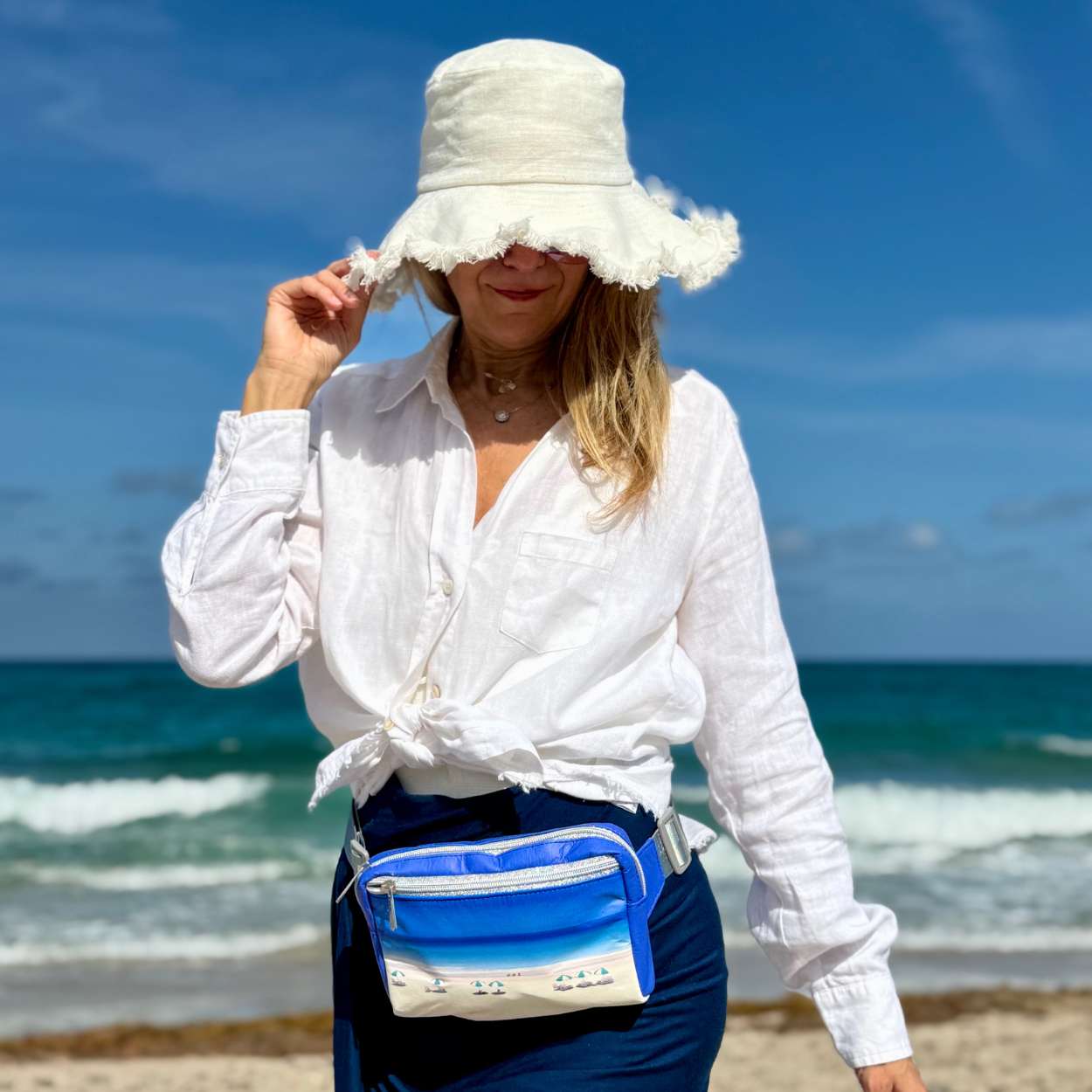 Woman on a beach wearing a white hat and white shirt with puffer crossbody fanny pack belt bag on harbor island beach print 