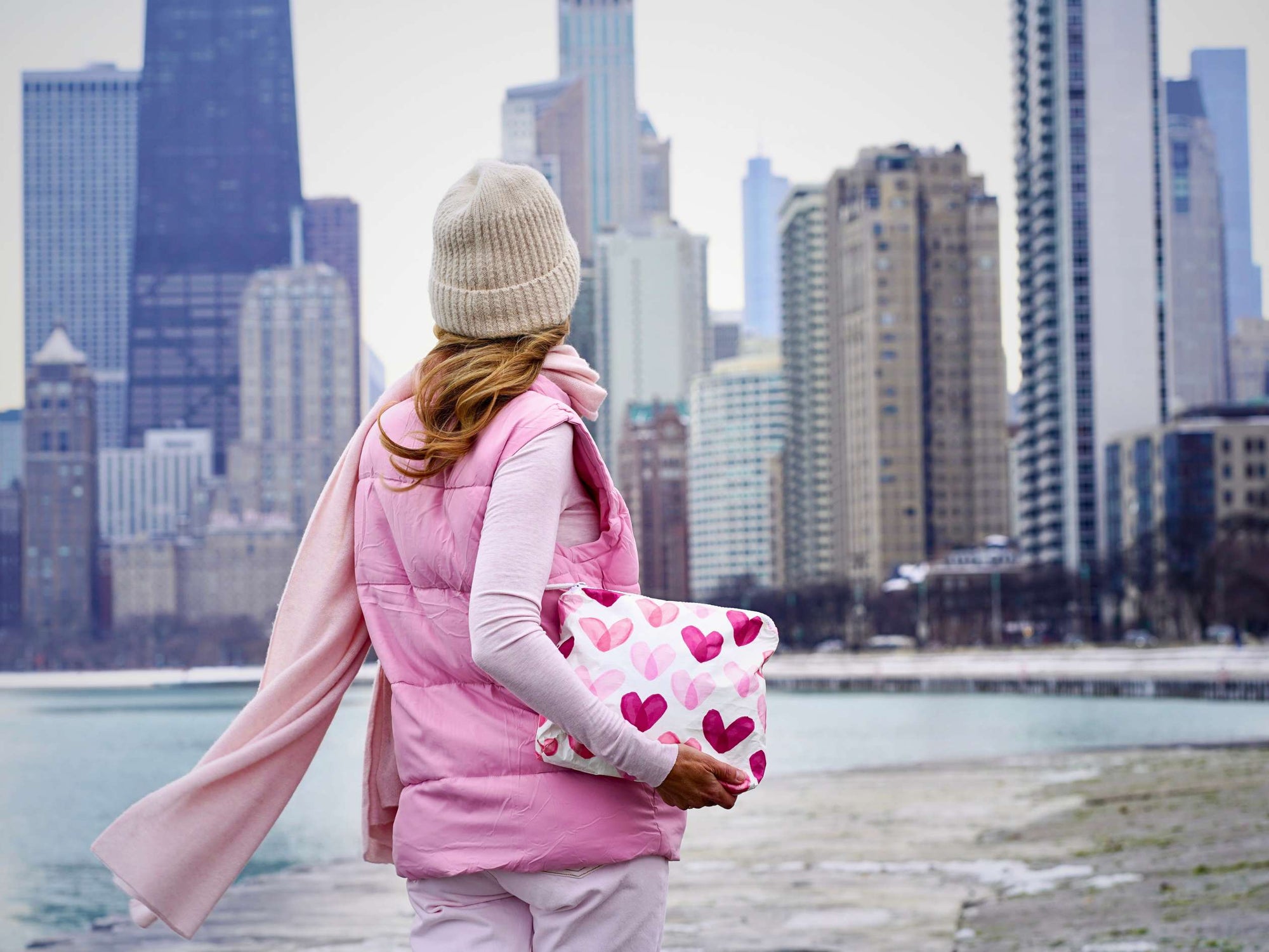 Person wearing a pink vest and holding a heart-patterned bag with a city skyline in the background