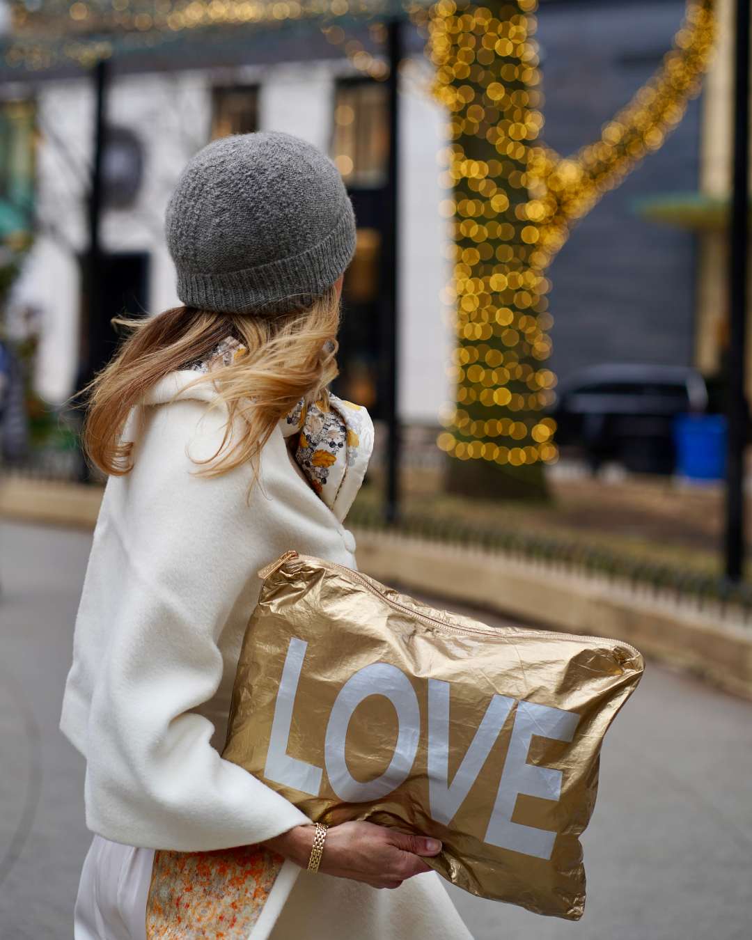 Woman holding a large zipper pouch with 'LOVE' printed 
with festive lights in the background