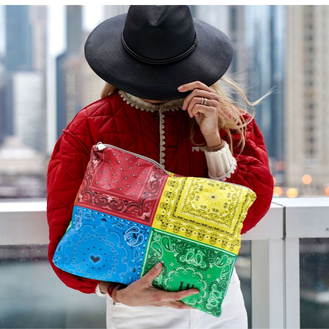 Person holding a colorful patchwork bandana clutch with a cityscape background