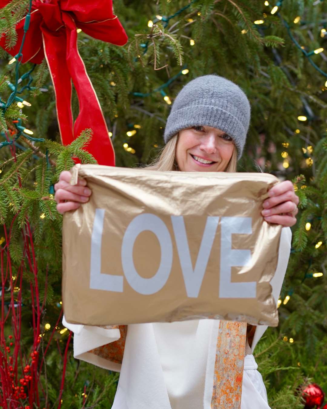 Woman holding a large zipper pouch with LOVE printing in front of a decorated Christmas tree