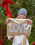 Woman holding a large zipper pouch with LOVE printing in front of a decorated Christmas tree