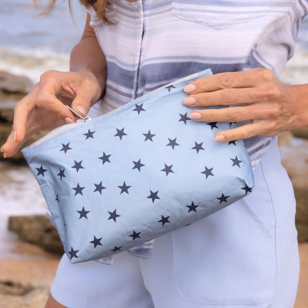 women holding a light blue with navy stars pouch unzipping it.
