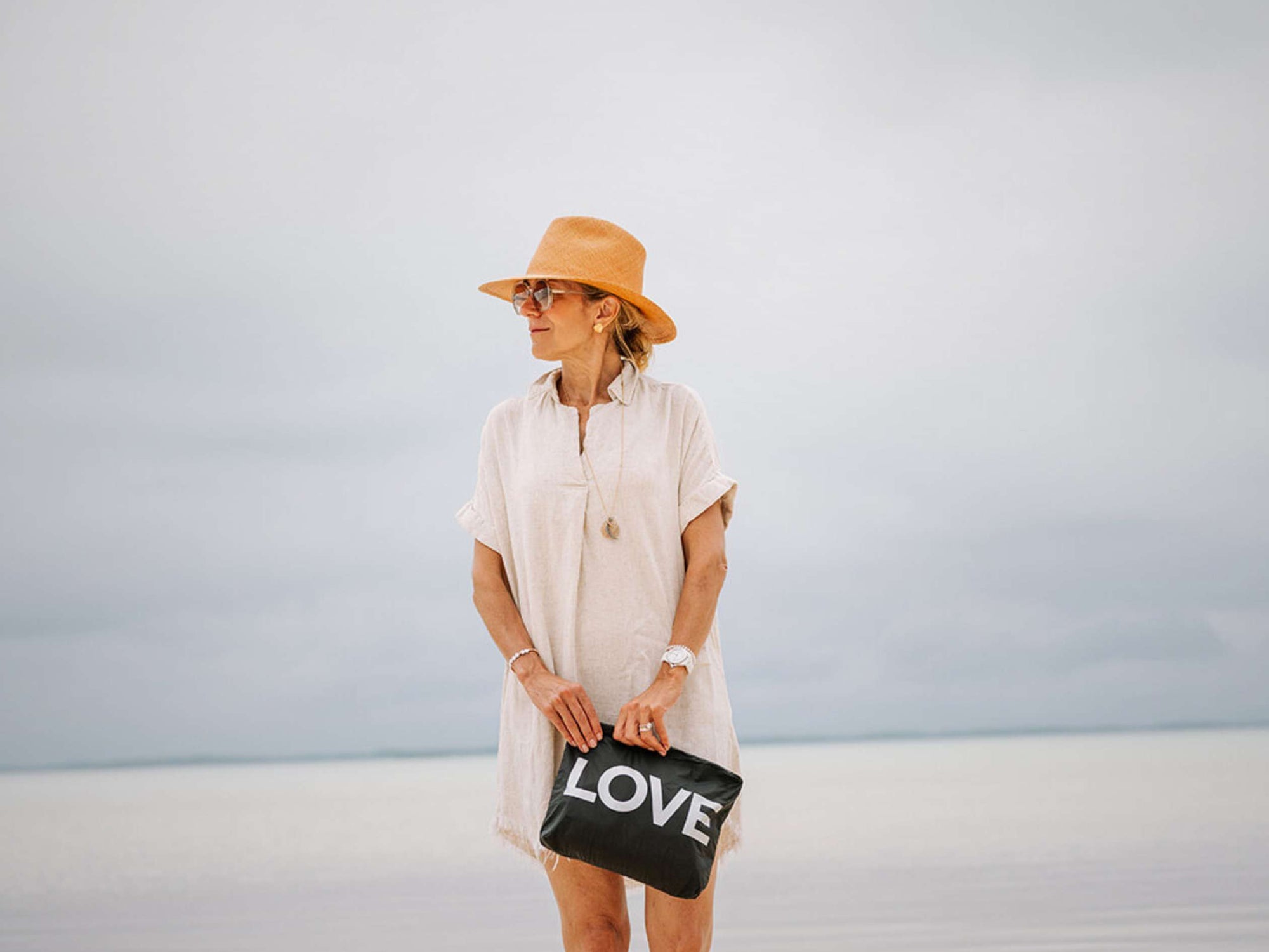 Woman holding a black bag with 'LOVE' on it against a light blue sky.