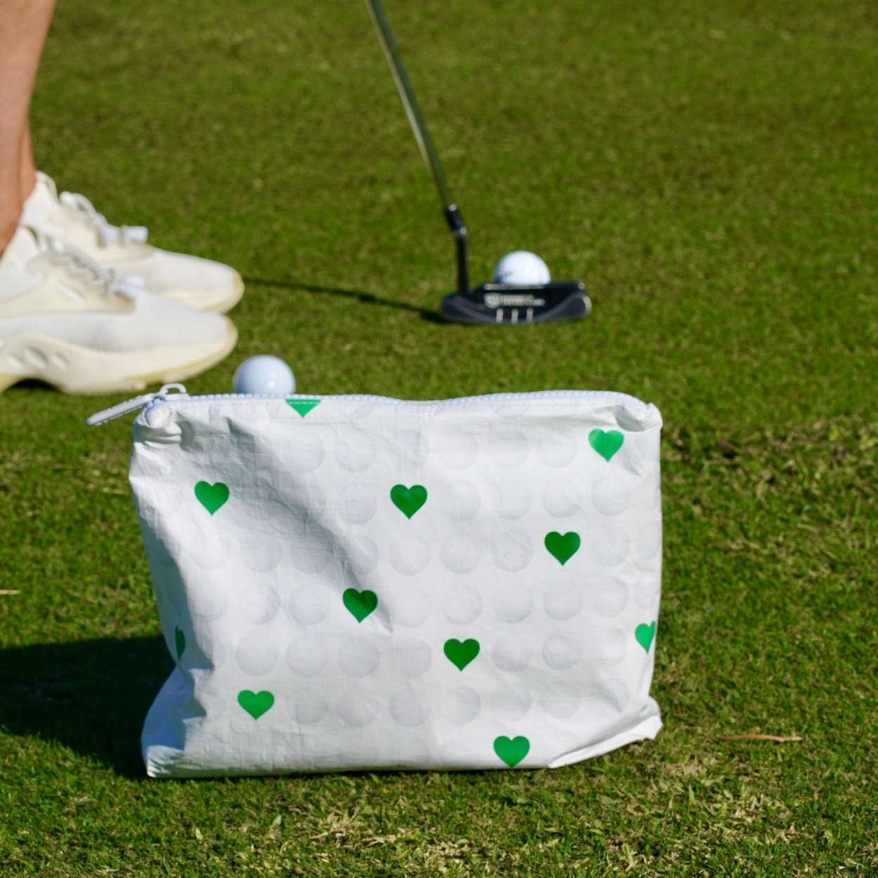 White pouch with white golf balls and green hearts on a golf course