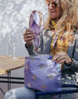 Woman holding a purple bag with star patterns and a pair of purple shoes outdoors.