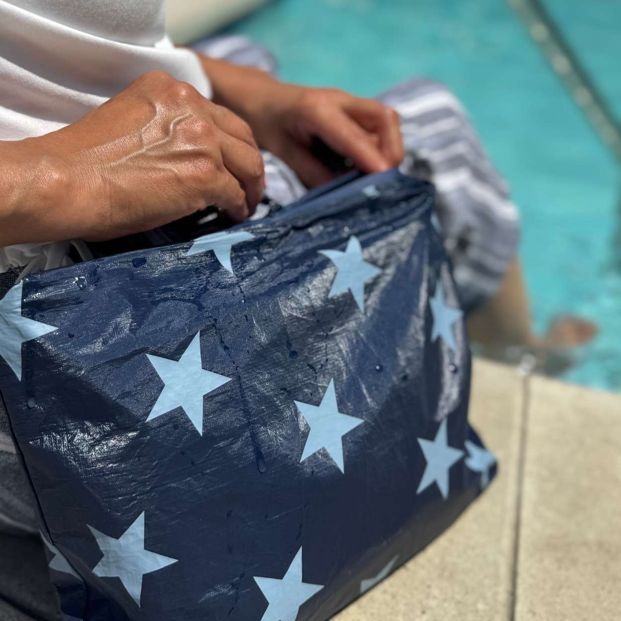 Person sitting by pool unzipping medium zipper pouch in shimmer navy with multi light blue stars