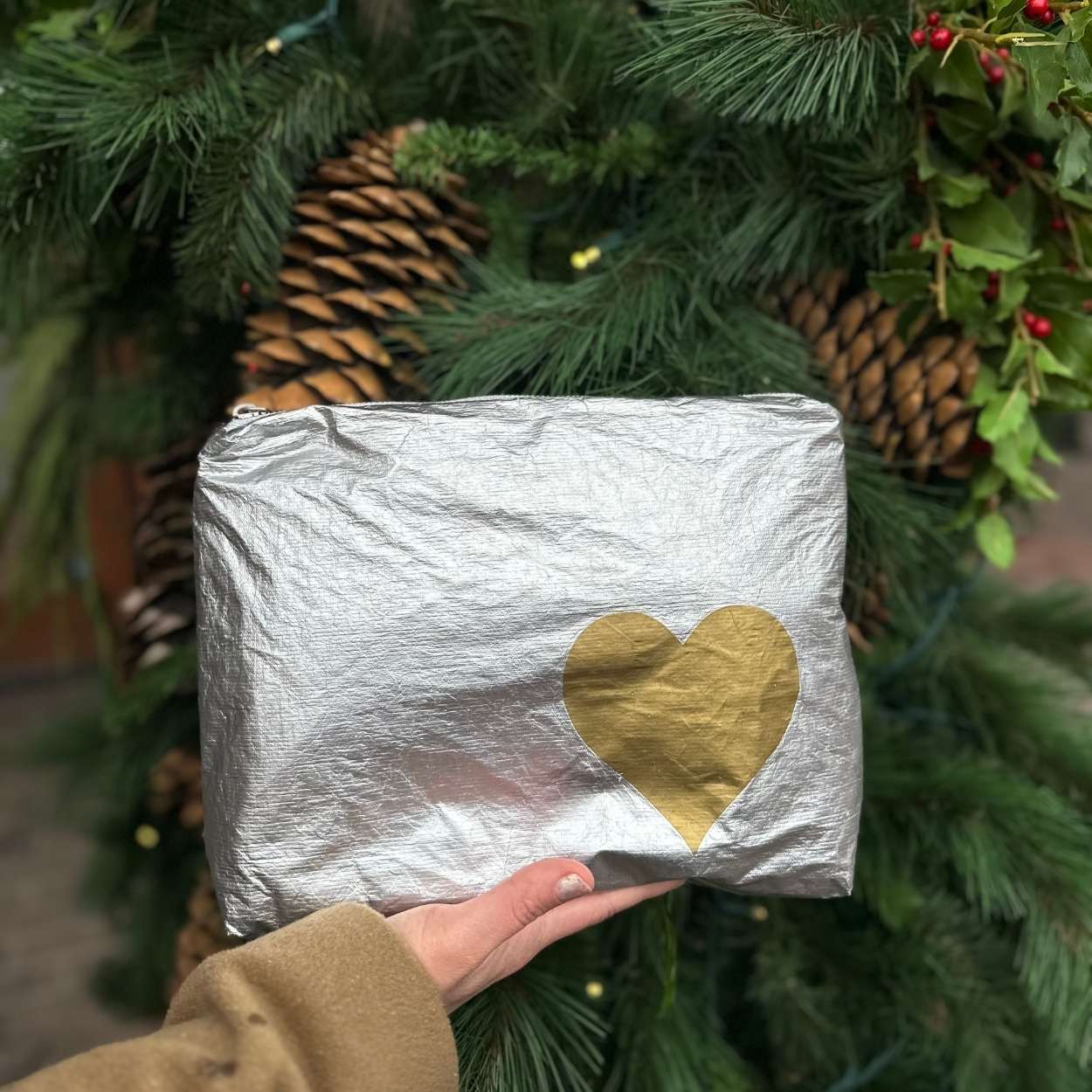 Person holding medium zipper pouch in silver with gold heart with pine background