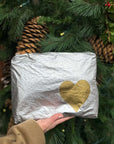 Person holding medium zipper pouch in silver with gold heart with pine background