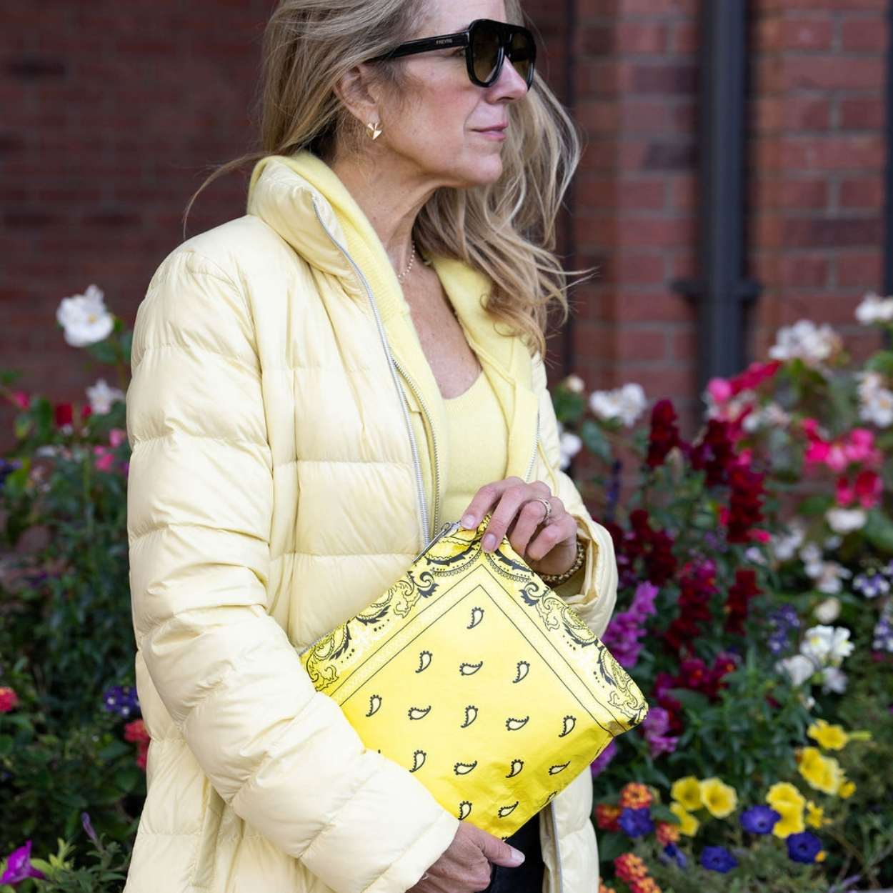 Woman in yellow jacket holding medium zipper pouch in yellow paisley bandana print