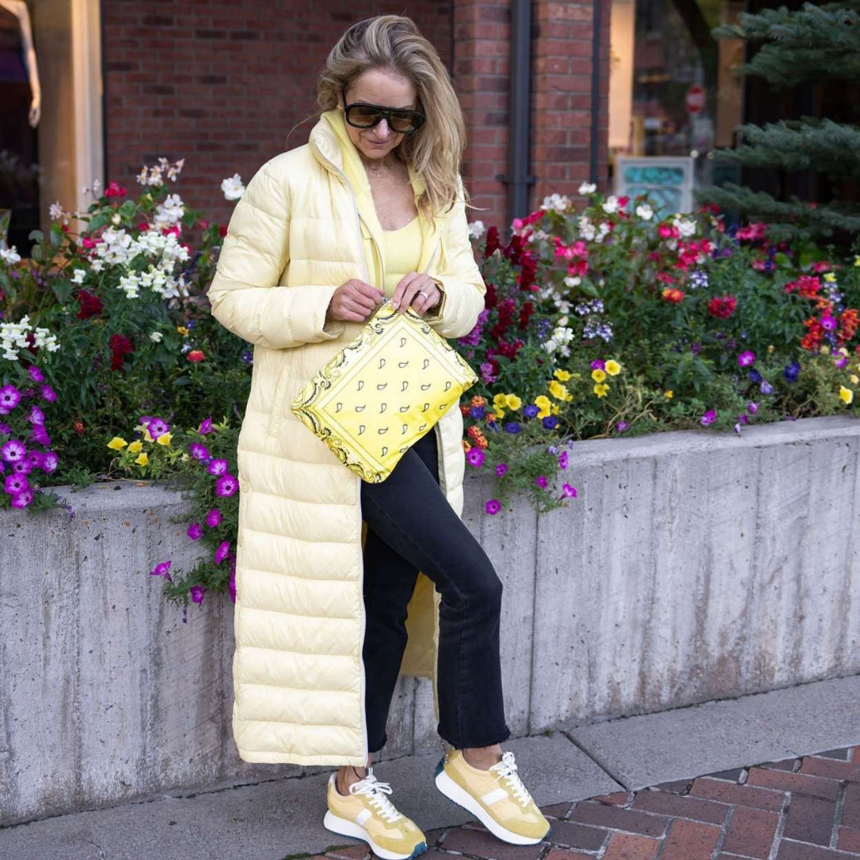 Women in long yellow jacket outdoors holding medium zipper pouch in yellow bandana print
