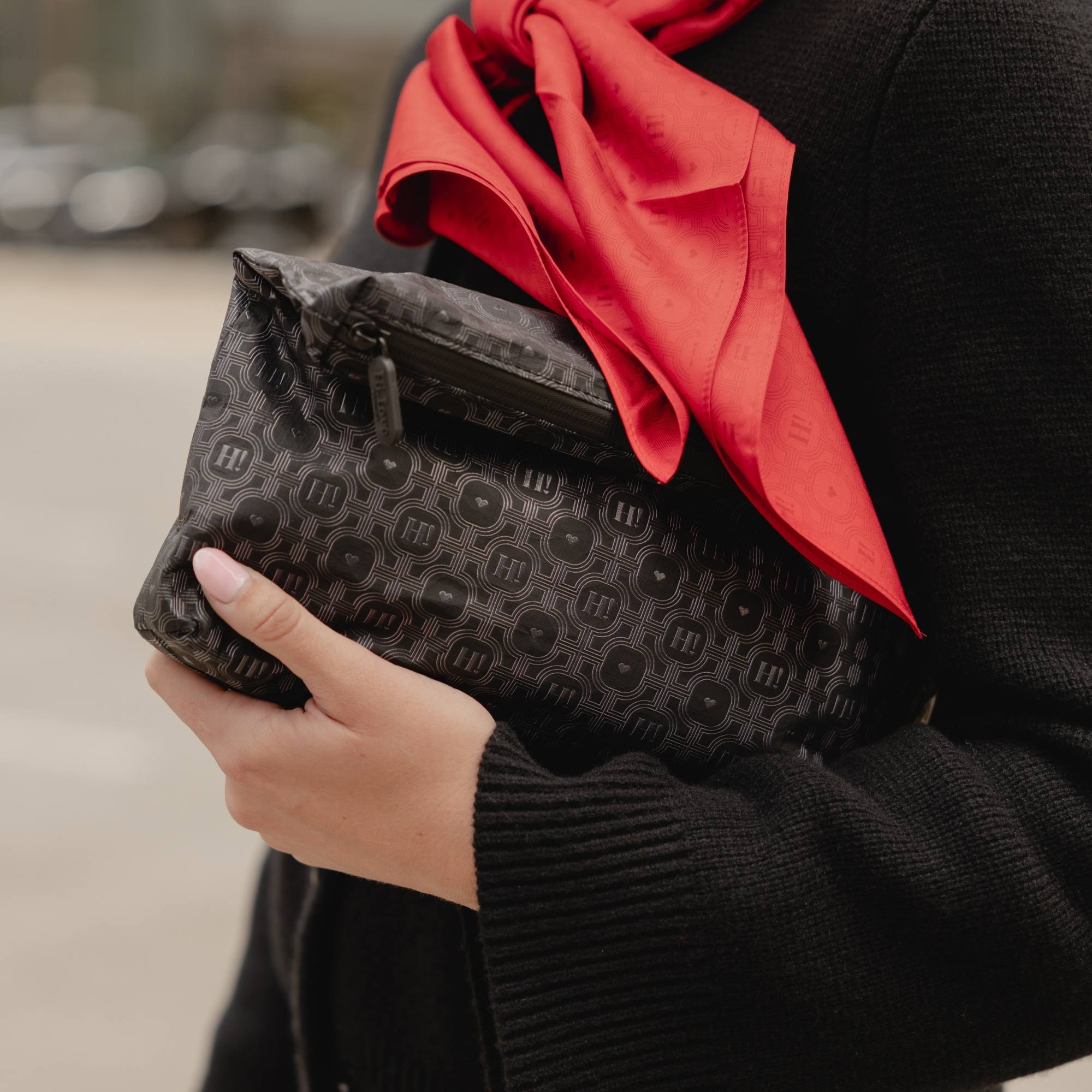 Woman holding a black signature medium zipper pouch with tonal Hi Love monogram print and a red scarf.