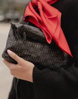 Woman holding a black signature medium zipper pouch with tonal Hi Love monogram print and a red scarf.