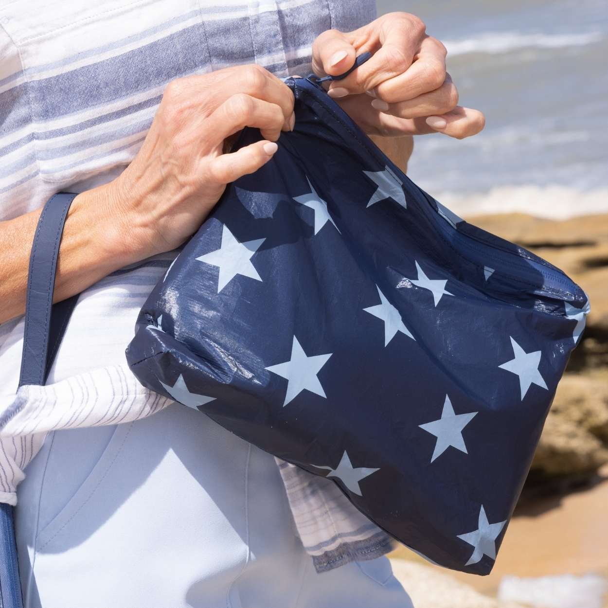 person unzipping zipper pouch that is a shimmer navy with light blue stars.