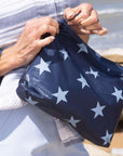 person unzipping zipper pouch that is a shimmer navy with light blue stars.