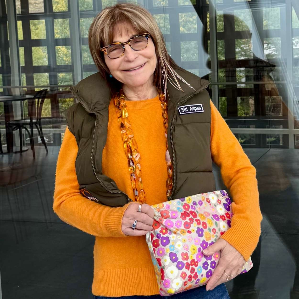Woman in orange sweater and vest holding medium zipper pouch in watercolor poppy print