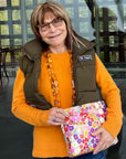 Woman in orange sweater and vest holding medium zipper pouch in watercolor poppy print