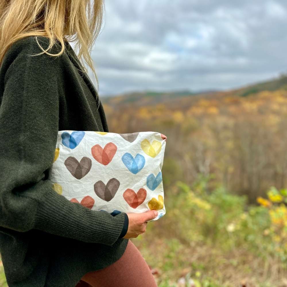 woman carrying clutch zipper pouch with heart print in shades of blue bronze and yellow