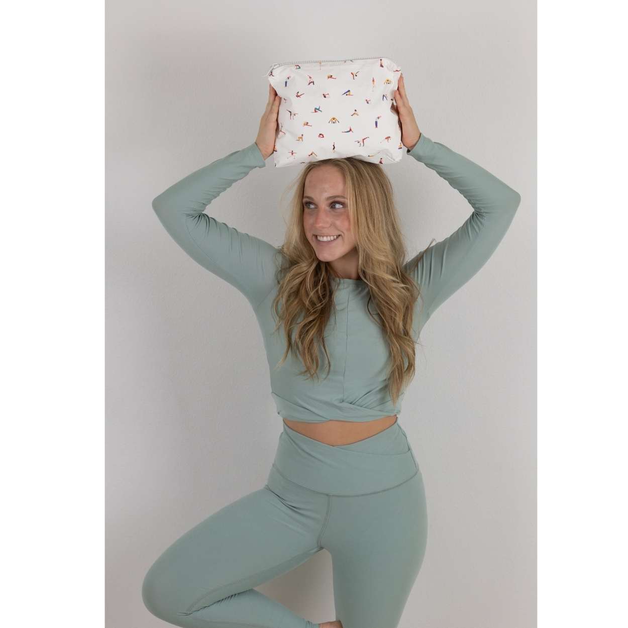 Woman in tree pose holding a Zipper Pouch with a colorful yoga poses print