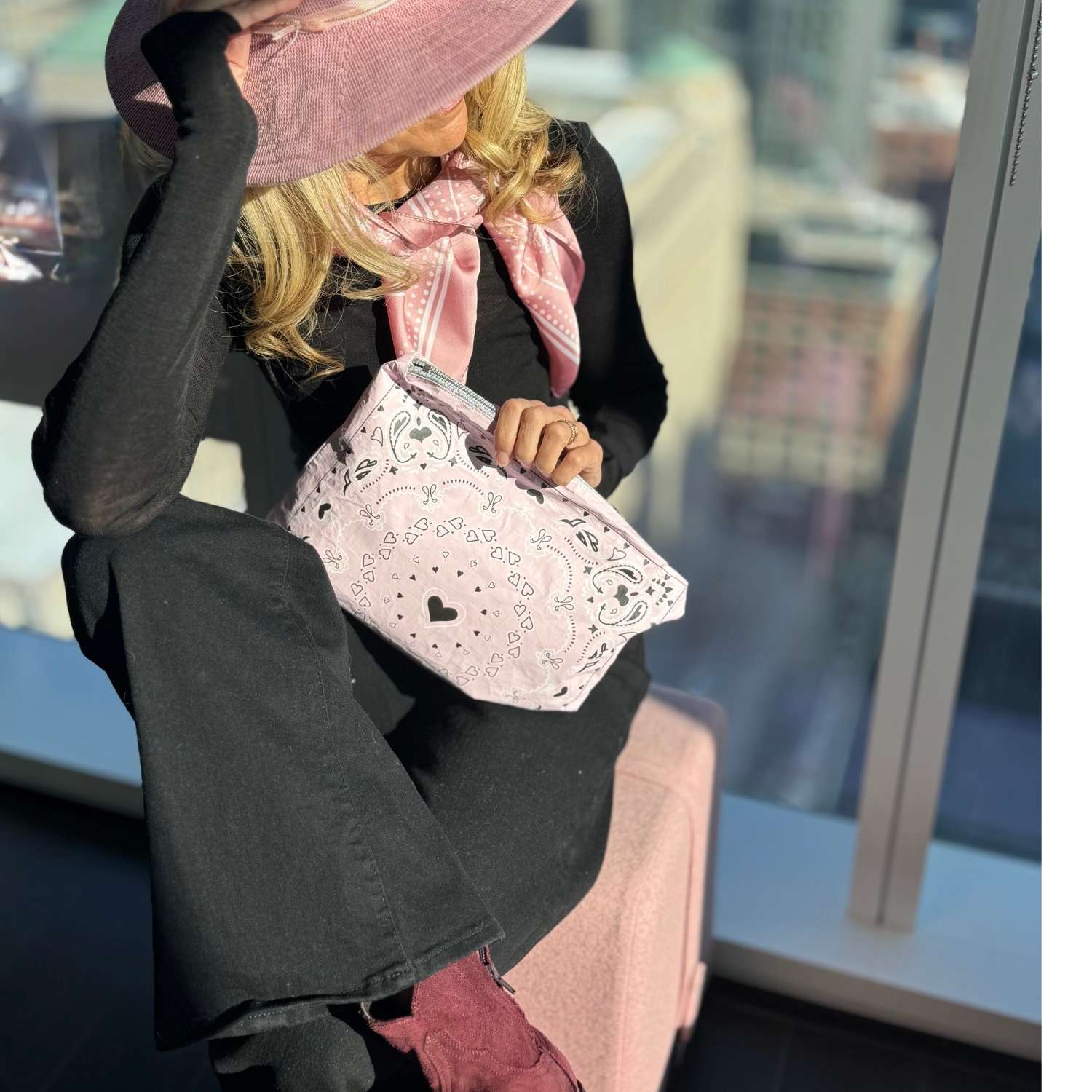 Person holding a pink handbag with a paisley bandana pattern, wearing a black outfit and pink shoes, in an indoor setting.