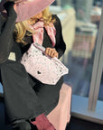 Person holding a pink handbag with a paisley bandana pattern, wearing a black outfit and pink shoes, in an indoor setting.