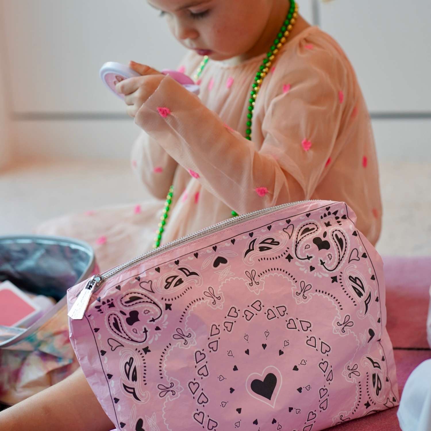 Child playing with a pink makeup bag featuring bandana heart designs.