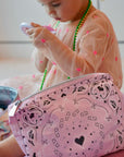 Child playing with a pink makeup bag featuring bandana heart designs.