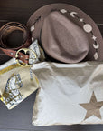 Cowboy hat, belt, silk scarf with horse design, and star-patterned bag on a wooden surface