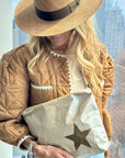 Person wearing a quilted jacket and straw hat, holding a beige bag with a star design.