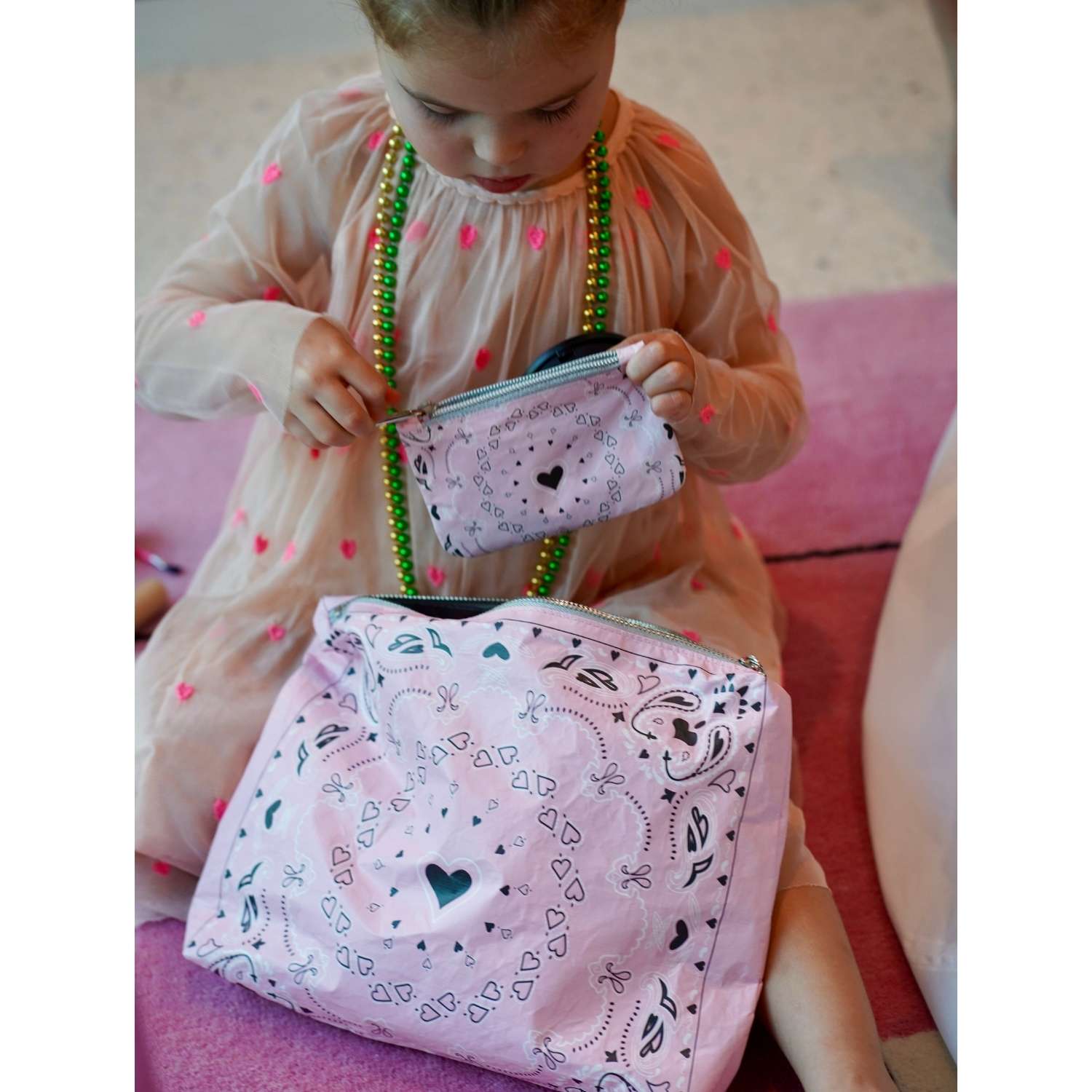 Little girl holding a pink pouch with paisley bandana heart patterns on a pink rug