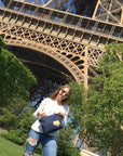 Person standing in front of the Eiffel Tower with trees and clear sky