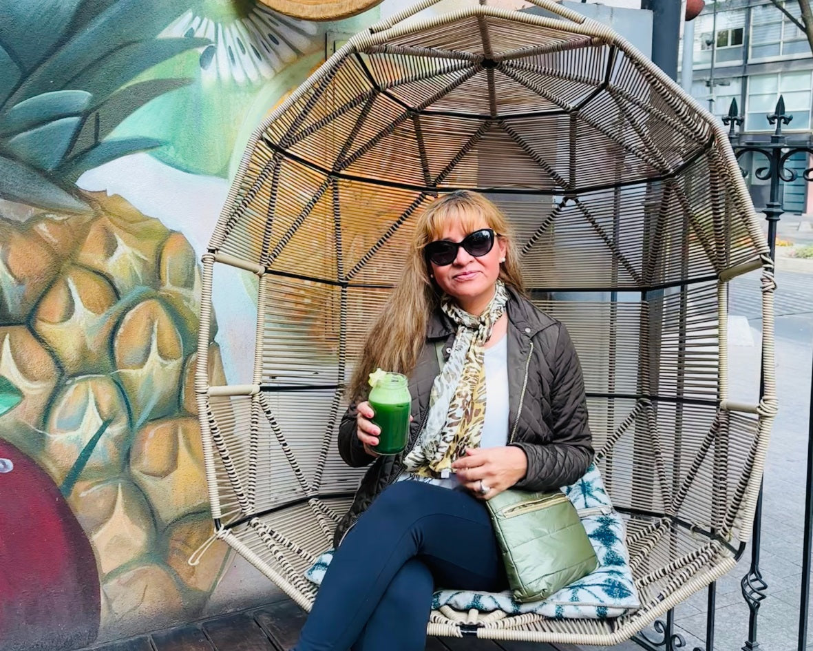 Woman sitting in outdoor chair holding a matcha and green crossbody purse with city background