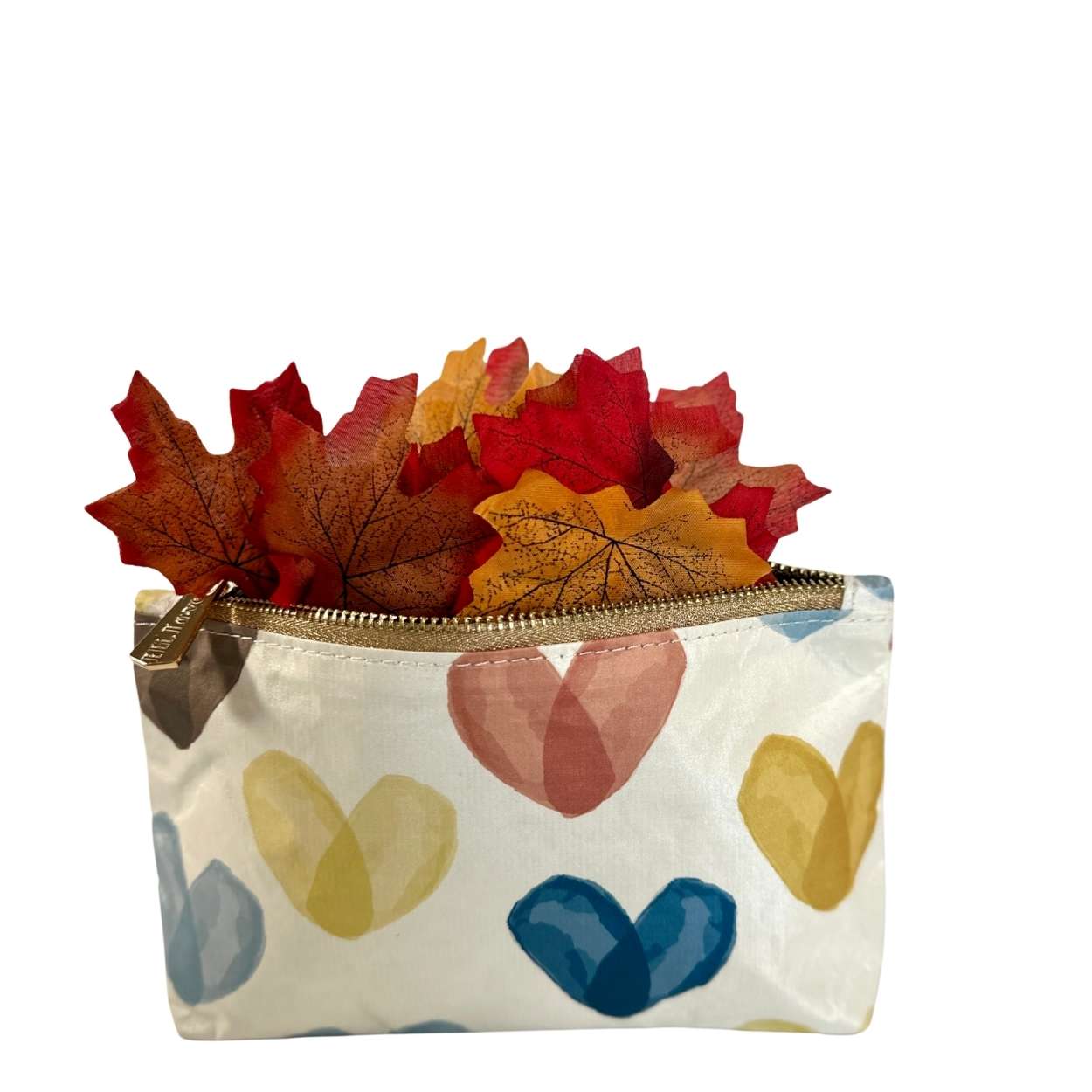 Small pouch with colorful heart patterns and a zipper, containing autumn leaves on a white background.