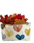 Small pouch with colorful heart patterns and a zipper, containing autumn leaves on a white background.