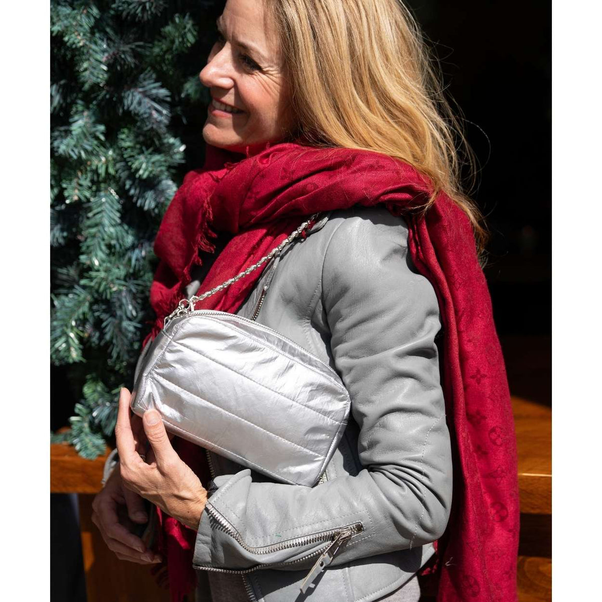 A woman wearing a gray jacket and a red patterned scarf carries a silver puffer crossbody bag with a chain strap.