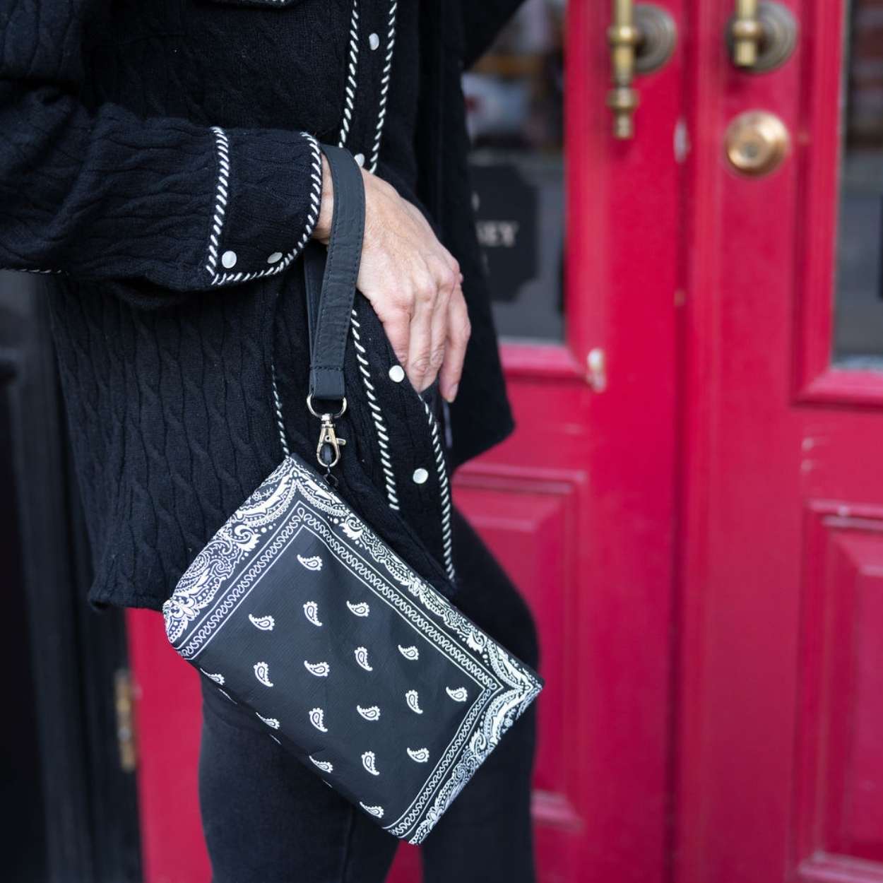 Person holding mini zipper pouch in black bandana print by red door