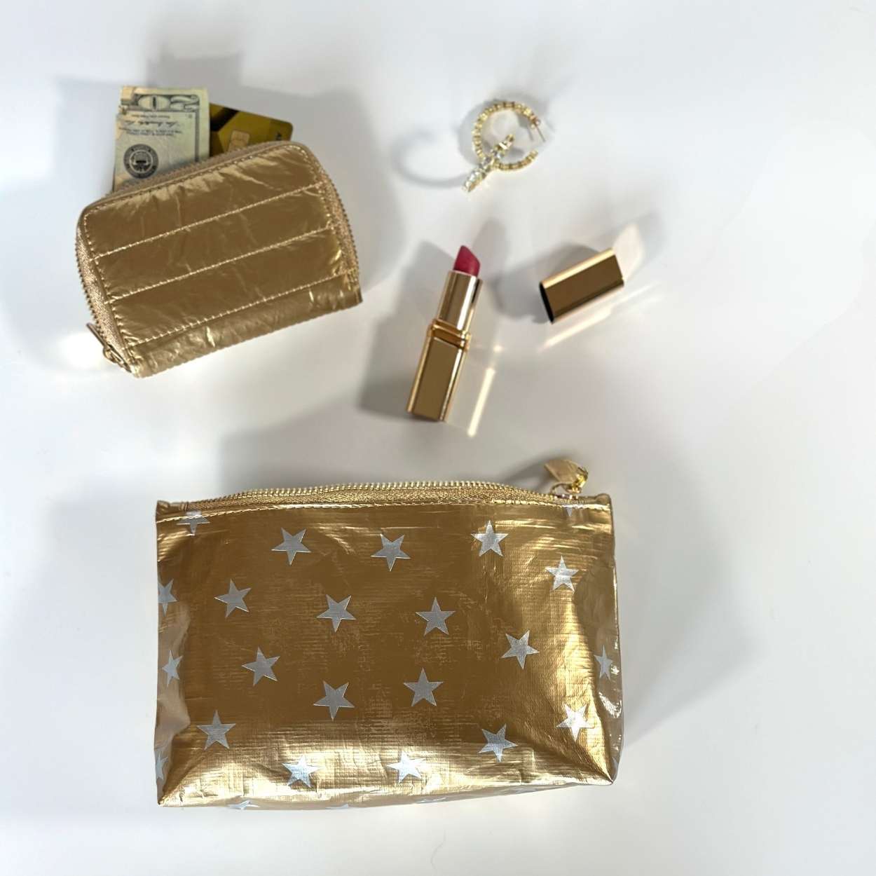 Mini zipper pouch in gold with myriad of stars and puffer wallet in gold with accessories on white background 