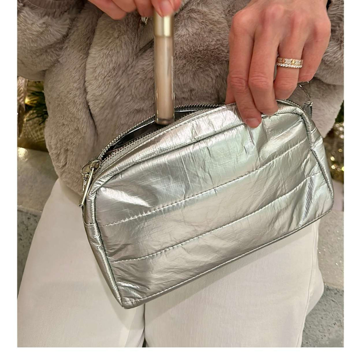 Silver Clutch shown putting lip gloss inside against a person wearing a light gray faux fur jacket.
