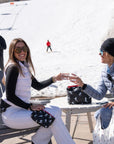 Two women enjoying apres ski with their zip pouches in black and white dancing skier print.